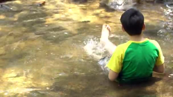 4K, молодий азіатський милий хлопчик сидить і грає в річці  . — стокове відео
