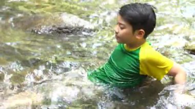 4k ,Genç asya sevimli çocuk oturup nehirde oynamak .