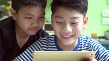 Genç mutlu Asyalı çocuk cep telefonu ve tablet bilgisayarla oyun oynuyor. .