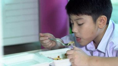 Asyalı çocuk öğrenci üniformalı plastik köpük kutusunda yemek yeme