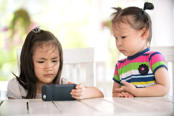 Två allvarliga asiatisk tjej sitter på stol ser mobilen — Stockfoto