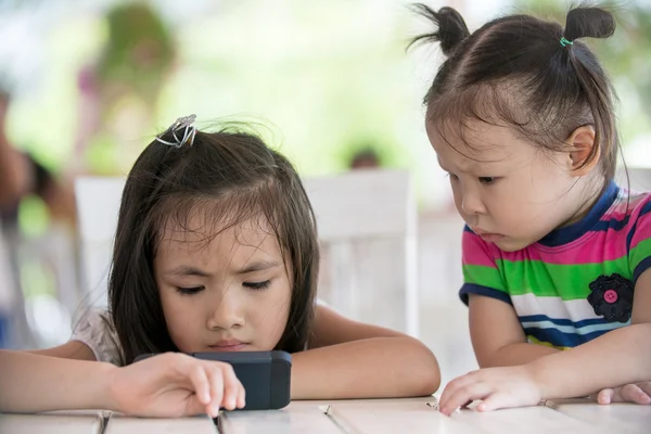 两个小的亚洲女孩坐在椅子上使用手机 — 图库照片