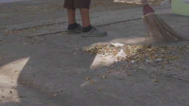 Asyalı hizmetçi Sonbaharda yere düşen yaprakları süpürüyor