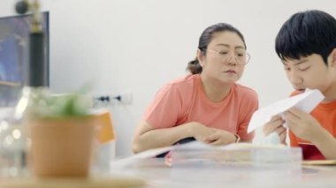 Asyalı bir anne oğluna dikiş atmayı öğretiyor, oğlu el işi yapıyor. Evde onunla..