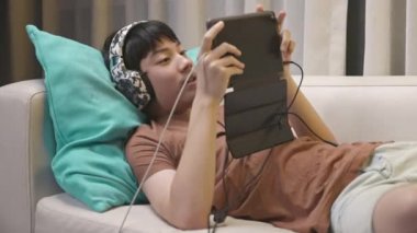 Genç çocuk çevrimiçi oyunlara bağımlıydı, uzanıp evdeki uzun bir kanepede tablet bilgisayar oynuyordu. Dolly vur.