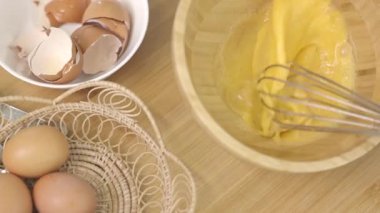 Kadın aşçı mutfak masasındaki ahşap kasede yumurta çırpıyor..