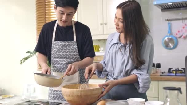 アジアのカップルパン屋を作るためにお互いを助けます自宅のキッチンでロマンチックな雰囲気の中で 若い人たちが一緒になって木の器に具材を混ぜ合わせ かき混ぜていきます — ストック動画