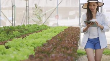 Akıllı çiftlik ve tarım teknolojisi kavramı. Mart genç Asyalı çiftçi seradaki organik bitki bahçesinin kalitesini ve miktarını kontrol etmek için tablet kullanıyor. .