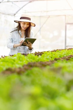 Akıllı çiftlik ve tarım teknolojisi kavramı. Mart genç Asyalı çiftçi seradaki organik bitki bahçesinin kalitesini ve miktarını kontrol etmek için tablet kullanıyor. .