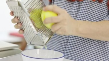Genç bir kadın mutfağında limon rendelemek için peynir rendesi kullanıyor..