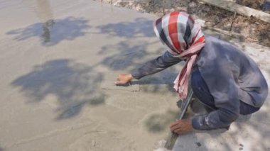 Beton yolun yüzeyini pürüzsüz ve güzel olması için ayarlayan işçinin arka görüntüsü. Beton yollar yapan isimsiz bir zanaatkar..