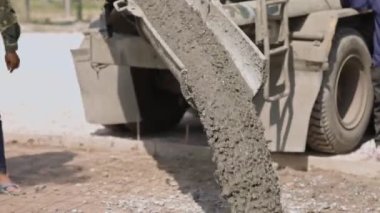 İşçiler çimento karıştırıcı kamyondan dökülen betonu yayıyor ve inşaat alanındaki yola sıvı beton döküyorlar..