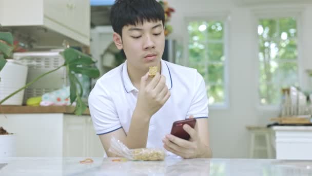 Asian Teen Boy Eating Snacks While Using Phone Same Time — Stock Video