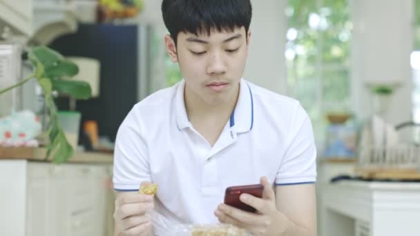Aziatische Tiener Jongen Eten Snacks Terwijl Het Gebruik Van Telefoon — Stockvideo