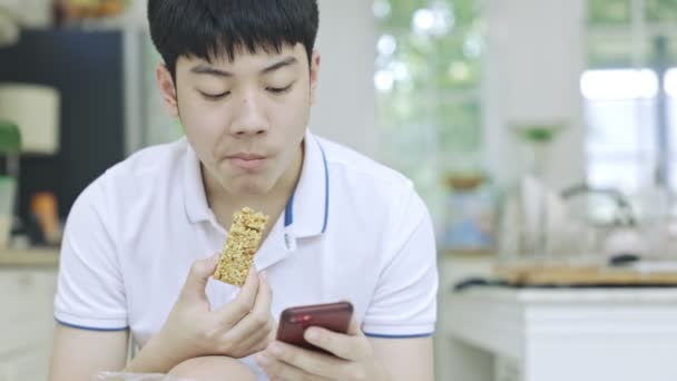 Asiatisch Teen Junge Eating Snacks Während Using Die Telefon Bei — Stockvideo