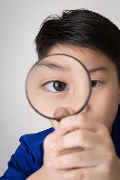 Porträtt av en ung asiatiska barn tittar genom ett förstoringsglas gla — Stockfoto