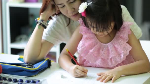 Pequeña chica asiática con la madre haciendo su tarea en la mesa — Vídeos de Stock