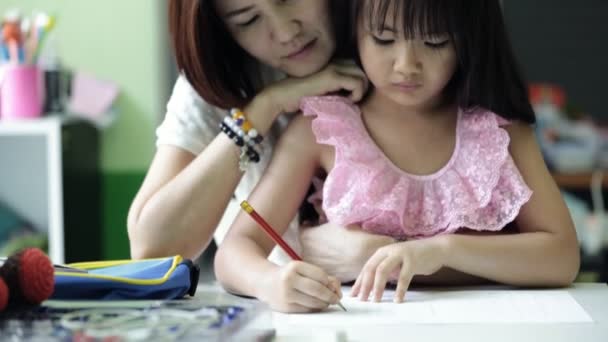 Pequeña chica asiática con la madre haciendo su tarea en la mesa — Vídeos de Stock