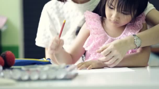 Pequeña chica asiática con la madre haciendo su tarea en la mesa — Vídeos de Stock