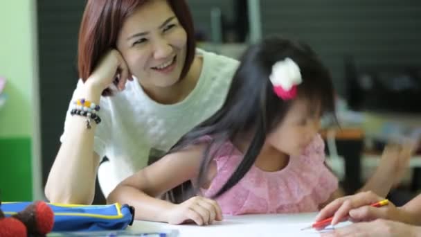 Menina asiática com a mãe fazendo seu dever de casa na mesa — Vídeo de Stock