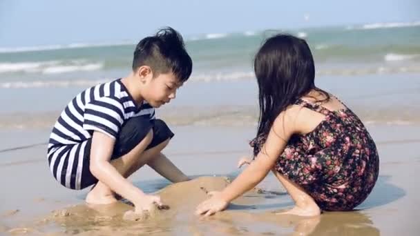 Primo piano di asiatico ragazzo e ragazza difficile a lavoro, costruzione castelli in il sabbia spiaggia — Video Stock