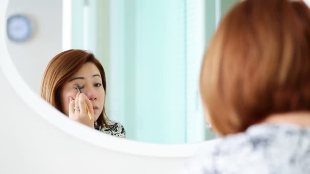 Femme asiatique appliquant le maquillage et regardant miroir dans la chambre . — Video