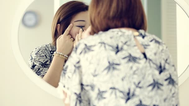Mujer asiática aplicando maquillaje y mirando el espejo en el dormitorio . — Vídeos de Stock