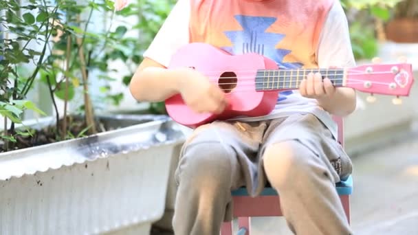 Little asian child sitting on mini chair and playing guitar — Stock Video