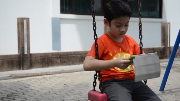 Asian cute boy playing tablet pc in the park at bright summer day — Stock Video