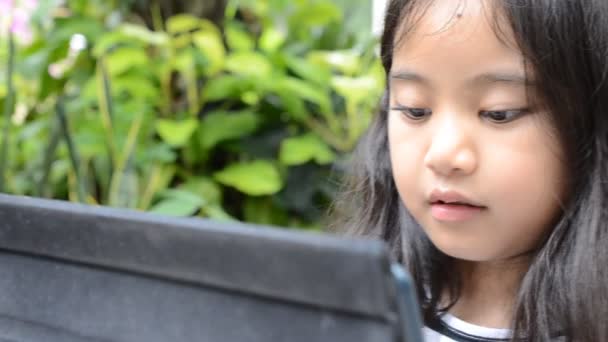 Kleine asiatische Mädchen spielen Tablet auf dem Tisch — Stockvideo