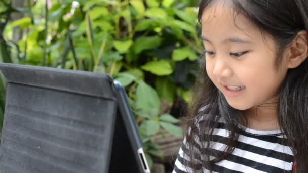 Маленькая азиатка играет на планшете на столе — стоковое видео