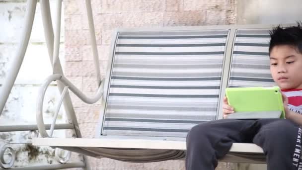 Asiático lindo chico jugando tableta pc en el parque en brillante día de verano — Vídeos de Stock