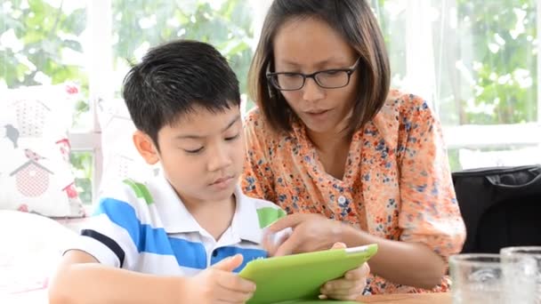 Asiático niño picos sus niños pequeños atención con algo en una tableta electrónica con la madre — Vídeos de Stock