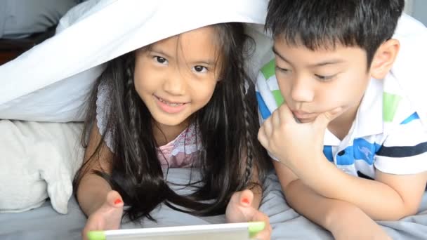Азиатская девочка и мальчик играют на планшете на кровати — стоковое видео