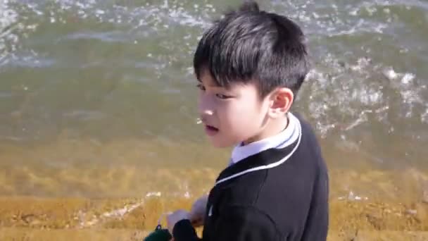 asiatisches Kind gibt Almosen für Fische am Fluss, kämpft um den Futterwurf von Menschen