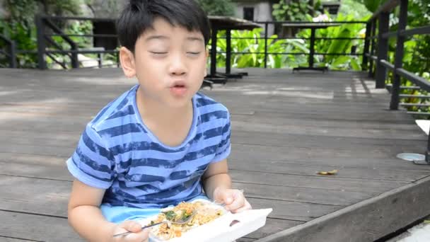 Jeune garçon mignon asiatique mangeant des nouilles chinoises frites., dans une boîte en mousse — Video