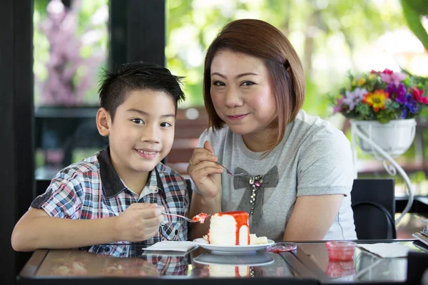 Asian mother with son eating cake in living room