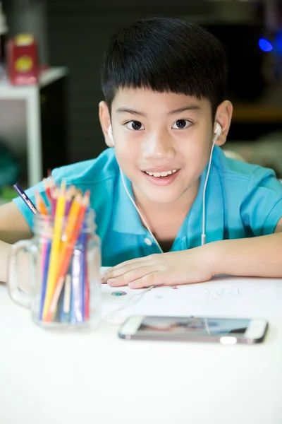 Een jongen met behulp van cellphone en schilderen op een wit papier thuis — Stockfoto