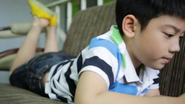 Asyalı çocuk evde kanepede uzanmış iken dijital bir cep telefonu kullanarak.