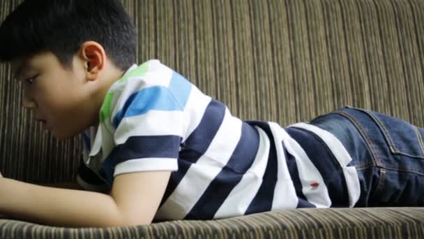 Ασιατικές παιδί, χρησιμοποιώντας ένα ψηφιακό τηλέφωνο κυττάρων ενώ ξαπλωμένη στον καναπέ στο σπίτι. — Αρχείο Βίντεο