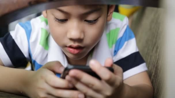 Asiático criança usando um telefone celular digital enquanto deitado no sofá em casa . — Vídeo de Stock