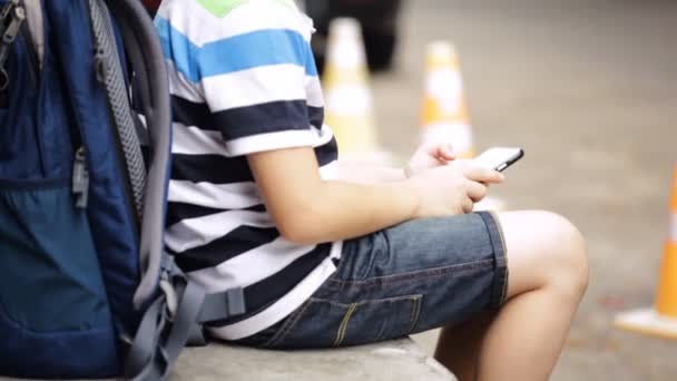 Niño asiático con mochila usando un teléfono celular digital — Vídeo de stock