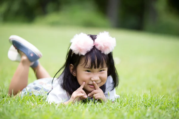 Pouco menina asiática jogando na grama verde no parque — Fotografia de Stock