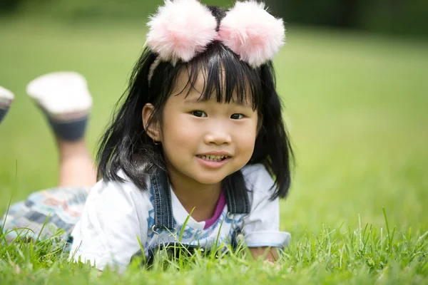 Pouco menina asiática jogando na grama verde no parque — Fotografia de Stock