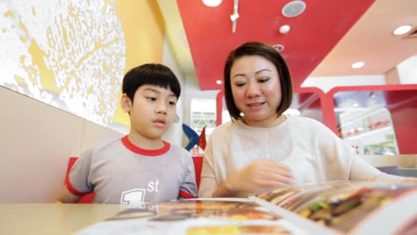 Ásia bonito menino com mãe leitura menu livro e ponto feliz rosto — Vídeo de Stock