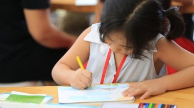 Küçük Asyalı kız masada bir resim çizim .
