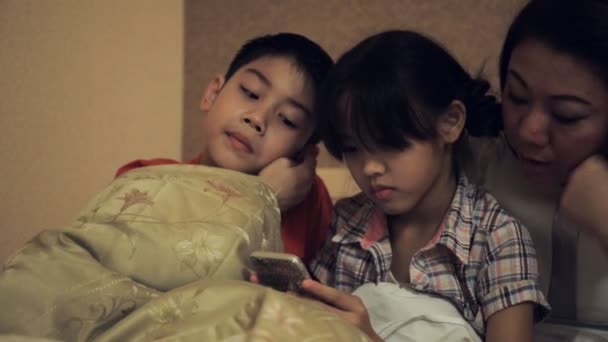 ベッド、寝室でスマートフォンでゲームをしながら楽しいアジアの家族を持っている幸せなアジアの家族 . — ストック動画