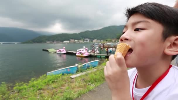 Jovem asiático menino comer gelo cream.with lago vista lateral, sorriso rosto . — Vídeo de Stock