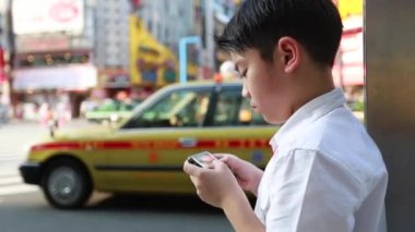 Tokyo, Japonya, street yürüyüş yakınındaki akıllı cep telefonu kullanarak mutlu Asyalı çocuk