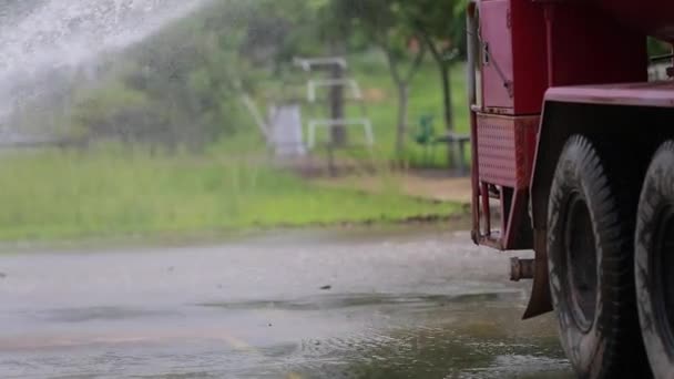 Неопознанный азиатский рабочий, использующий мощный распылитель шланга из грузовика-цистерны для мытья дороги — стоковое видео